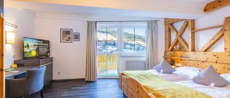 Habitación de hotel con una cama, un escritorio, una silla y vistas a un paisaje nevado a través de un ventanal grande.