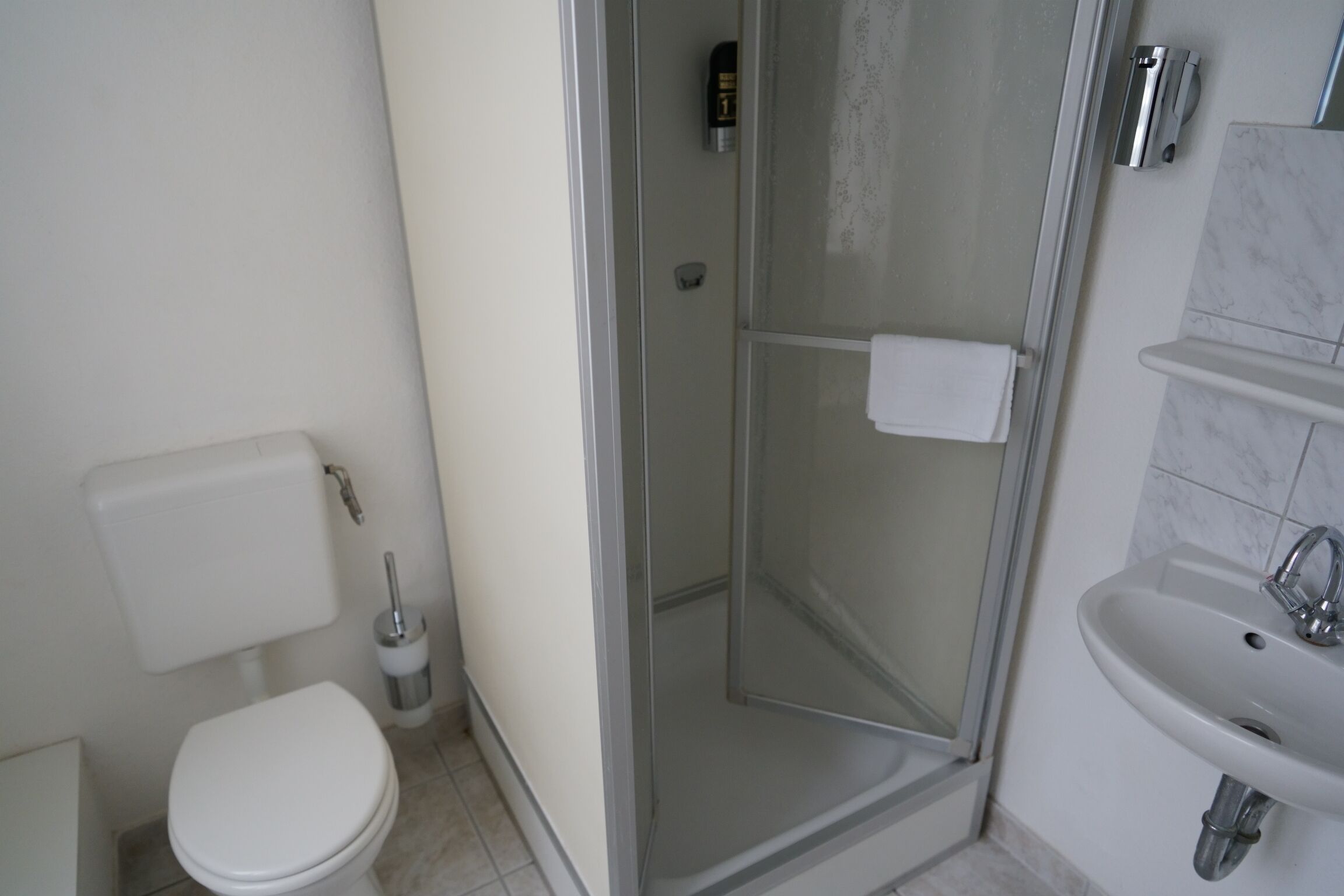 Un baño con inodoro, ducha con mampara de vidrio y lavamanos.