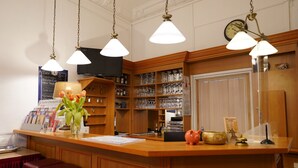 A reception area with a wooden counter, a clock, and a wall-mounted TV. - City Pension Berlin (Berlin)