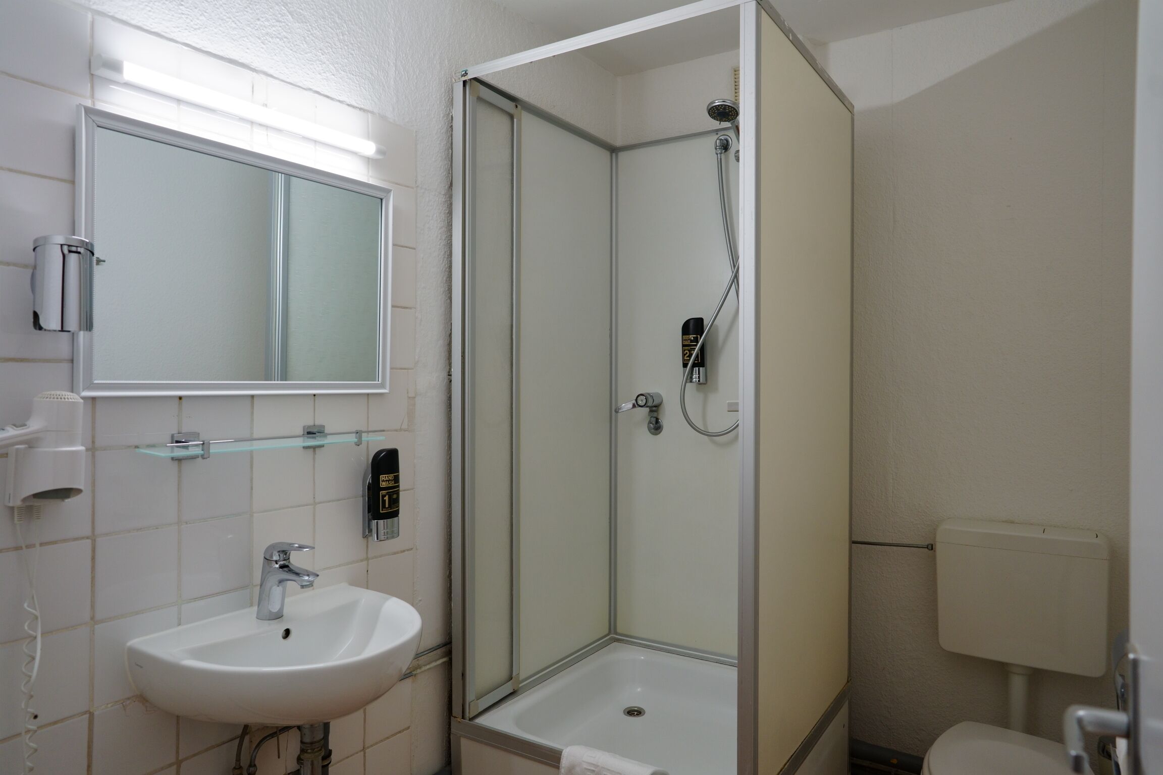 Baño con ducha envuelta en vidrio, lavamanos y retrete.