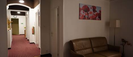A hotel room with a red carpeted hallway, a brown leather sofa, a small wooden table, and a painting on the wall.