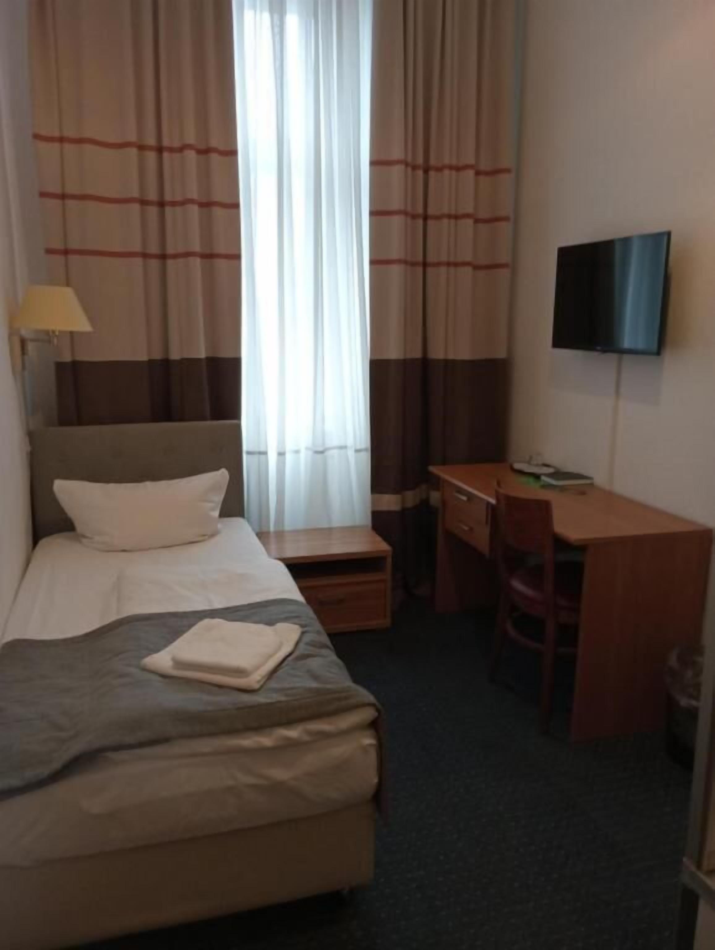 A hotel room with a bed, a desk, a chair, a TV, and curtains.