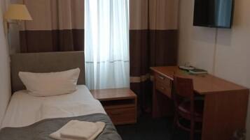 A hotel room with a bed, a desk, a chair, a TV, and curtains.