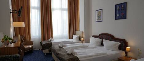 A hotel room with two beds, a desk, a chair, and a large window with curtains.