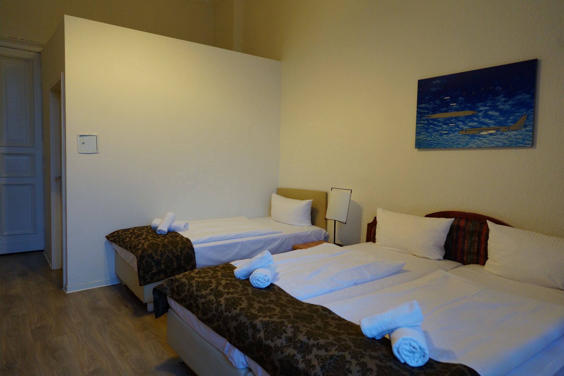 Ein Hotelzimmer mit zwei Betten, einem Bild an der Wand und einer Tür links.