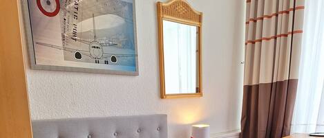 A hotel room with a bed, a nightstand, a lamp, a mirror, and a painting on the wall.