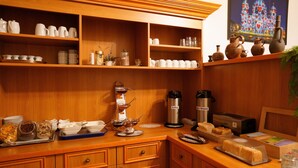 A kitchen with wooden cabinets, shelves with white mugs and cups, a coffee maker, a kettle, and a toaster. - City Pension Berlin (Berlin)