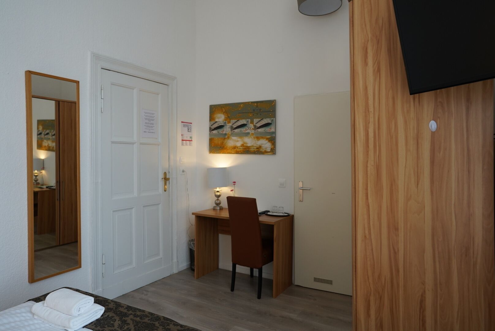 Ein Zimmer mit einem Bett, einem Schreibtisch mit Stuhl, einem Bild an der Wand und einer Tür.