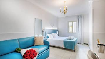 Una camera d'albergo con un divano blu, un letto con testiera blu, un comodino con una bottiglia di champagne e una finestra con tende.