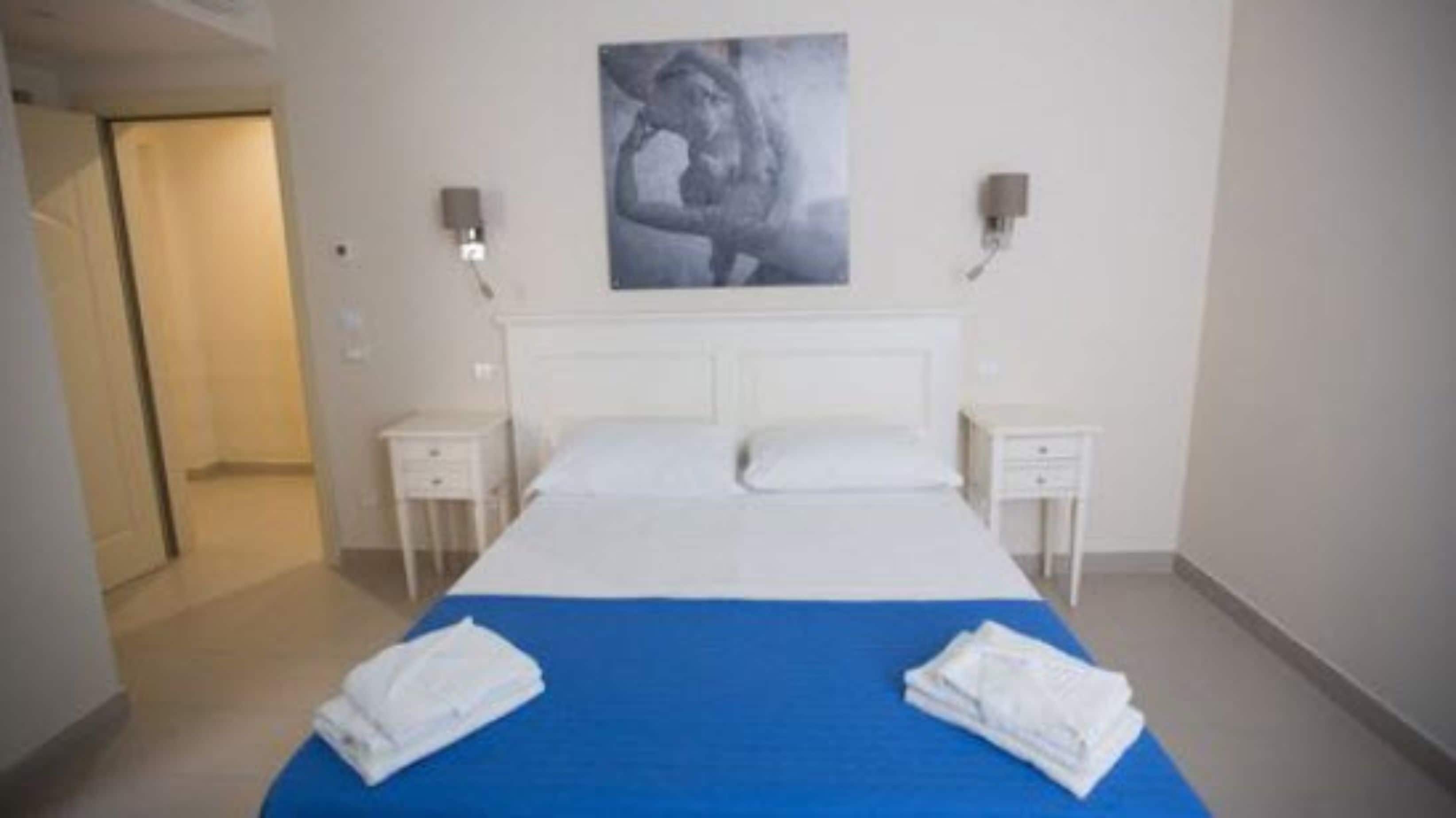 A hotel room with a bed, two bedside tables, a wall-mounted artwork, and a blue bedspread.