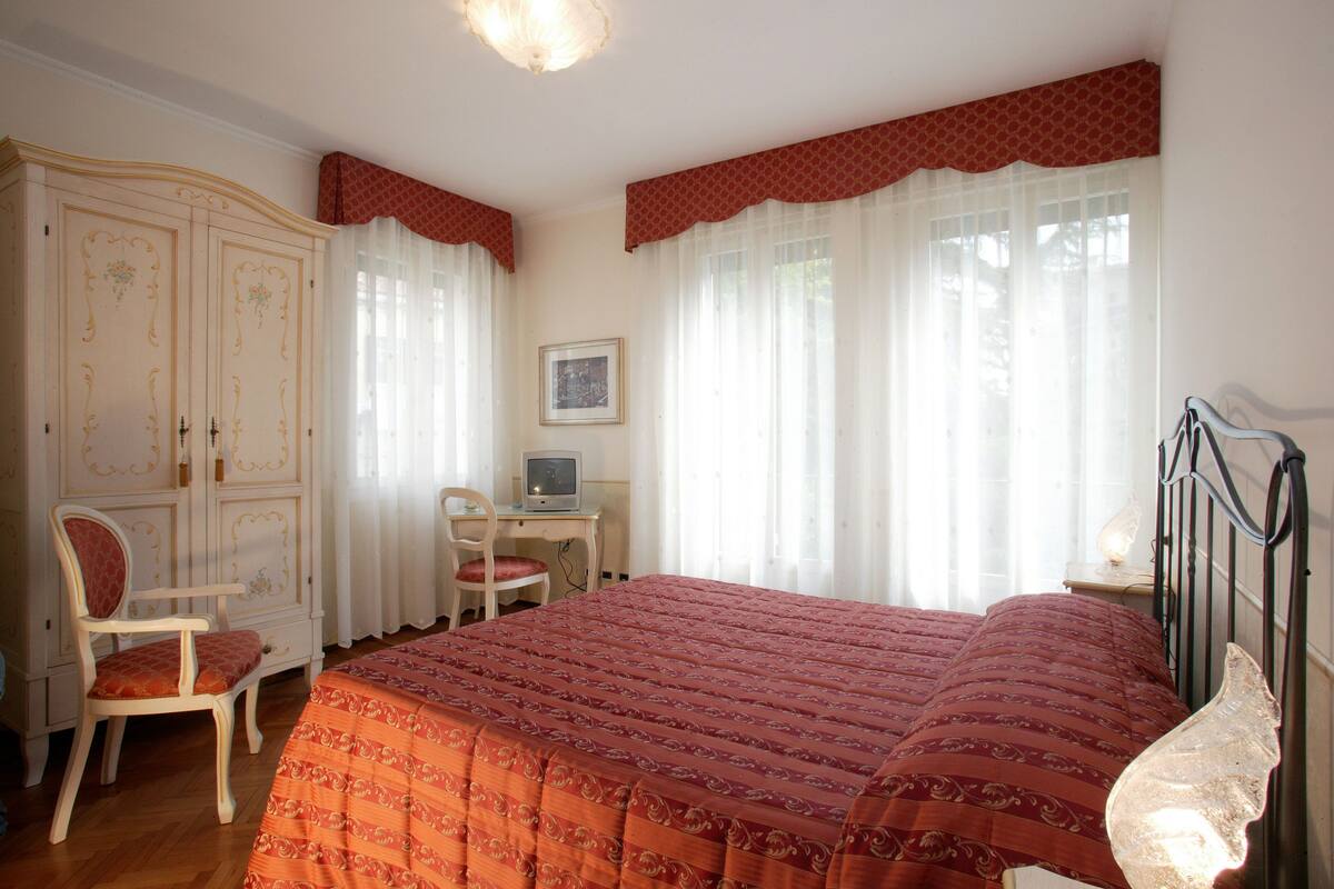 A bedroom with a large bed, a desk, a chair, and a wardrobe.