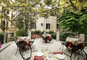 An outdoor dining area with tables set for two, surrounded by greenery and a building in the background. - Ca' San Rocco (Venice)
