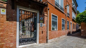 A narrow street with a building featuring a metal gate, brick walls, and a tiled roof. - Ca' San Rocco (Venice)