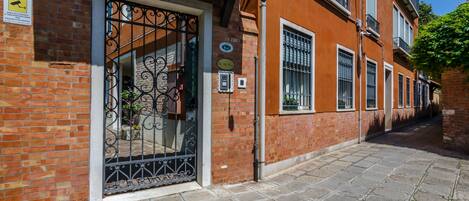 A narrow street with a building featuring a metal gate, brick walls, and a tiled roof.