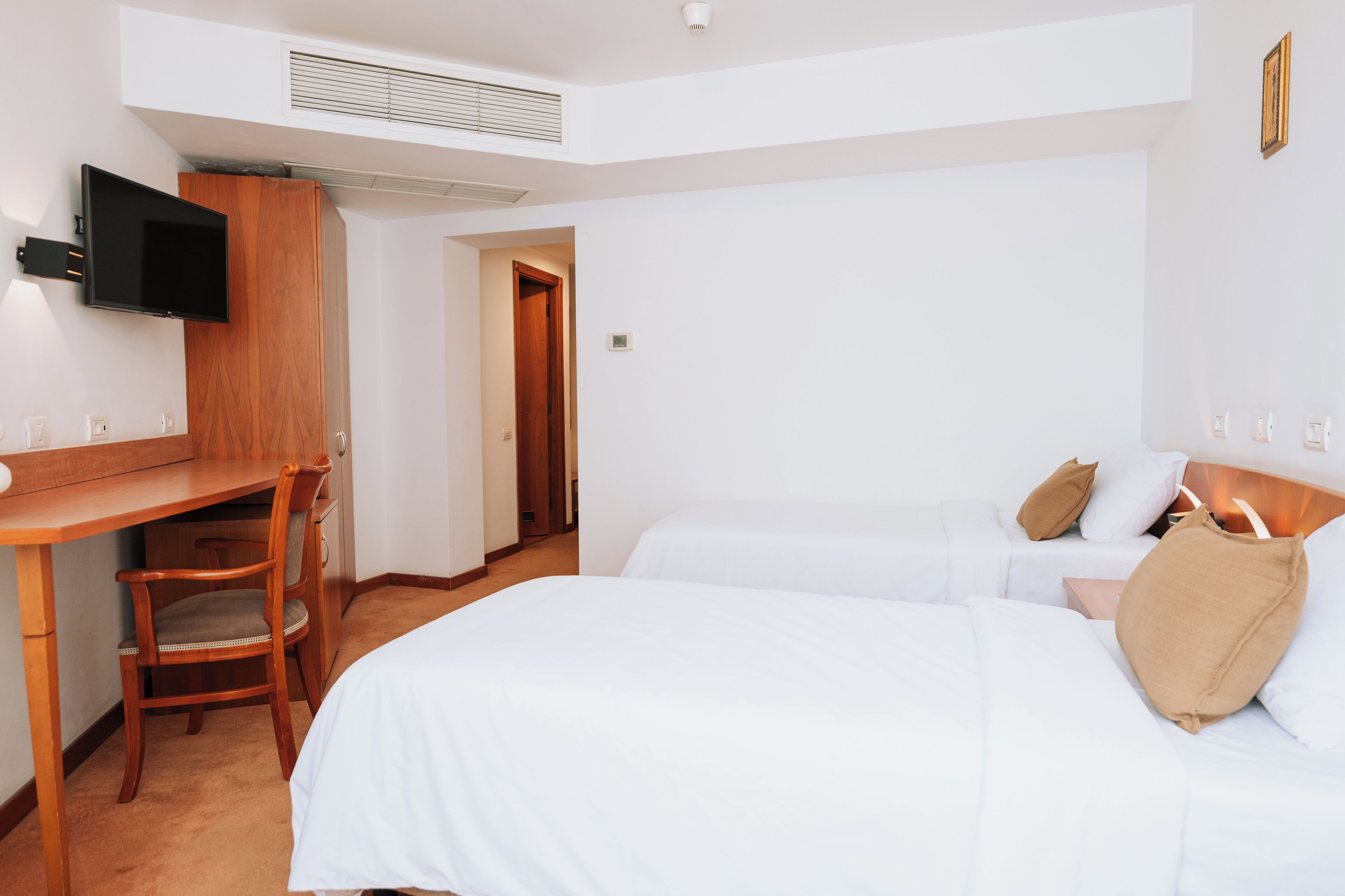 A hotel room with a bed, a desk, a chair, and a TV mounted on the wall.