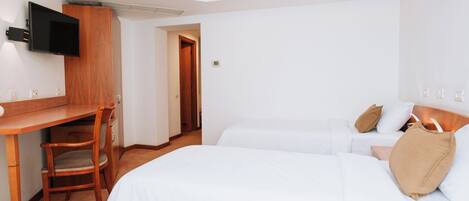 A hotel room with a bed, a desk, a chair, and a TV mounted on the wall.