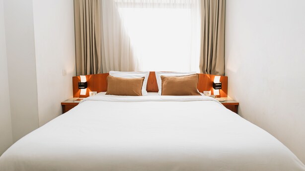 A hotel room with a large bed, two bedside tables, and a window with curtains.