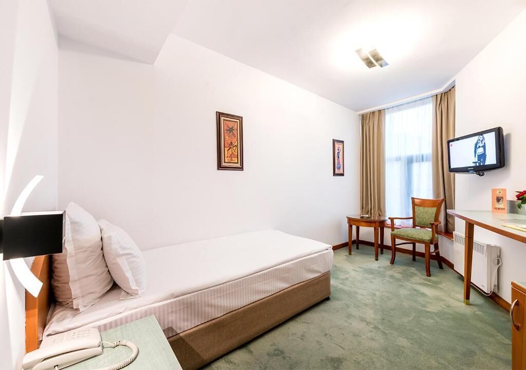 A compact hotel room with a single bed, a desk with a chair, a television, and two framed pictures on the wall.