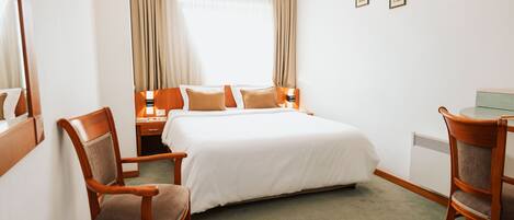 Una habitación de hotel con una cama grande, dos sillas de madera, una mesita y un escritorio.