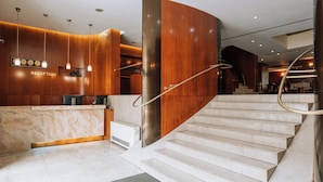 A modern reception area with a marble counter, wooden paneling, and a staircase with a handrail.