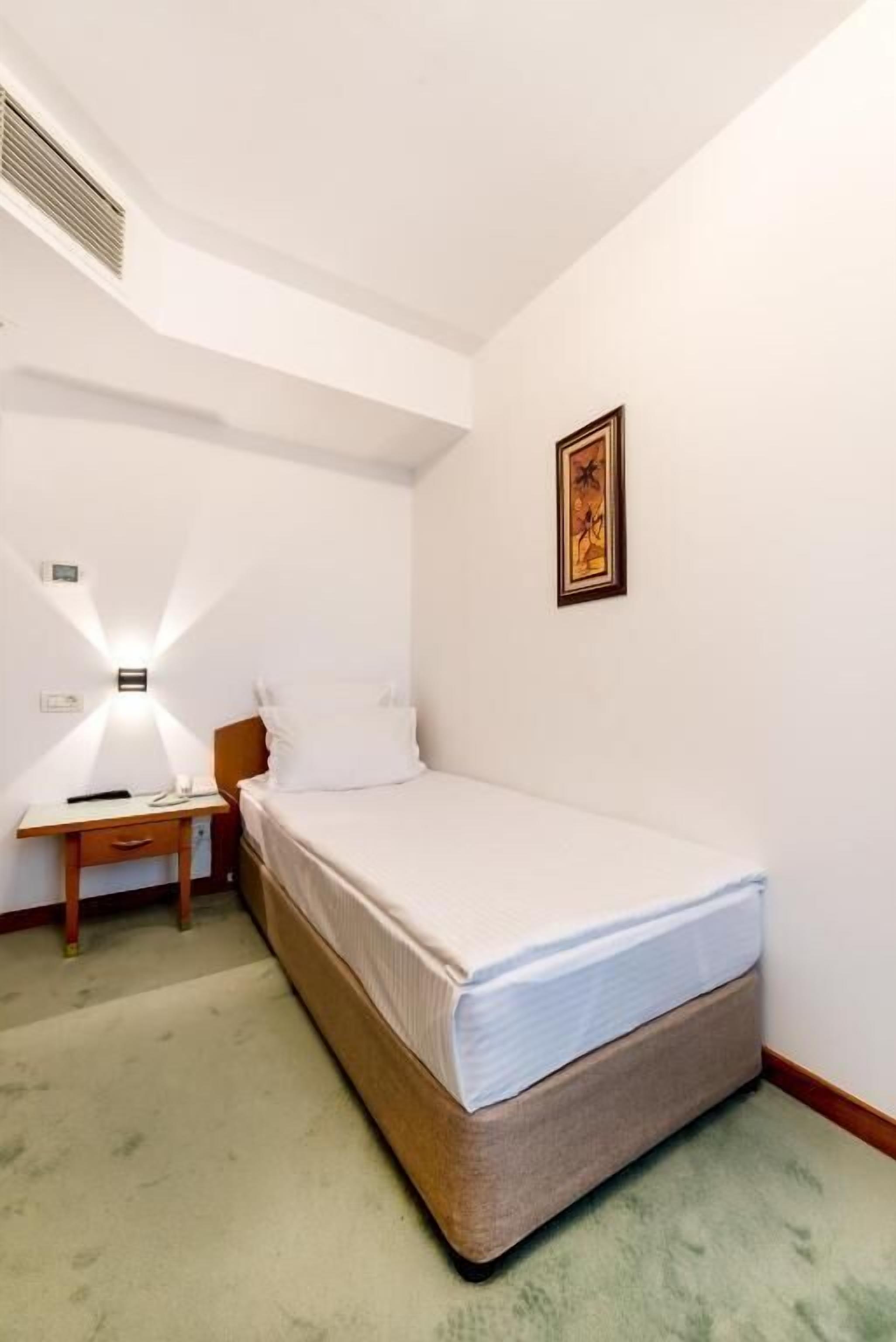 Una habitación pequeña y limpia con una cama individual, una mesita de noche y un cuadro colgado en la pared.