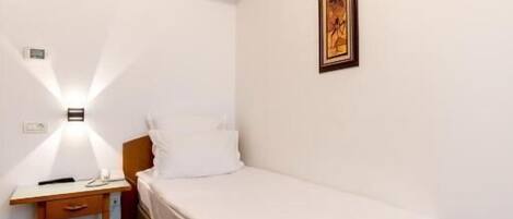 Una habitación pequeña y limpia con una cama individual, una mesita de noche y un cuadro colgado en la pared.