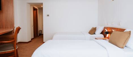 A hotel room with a large bed, a desk, and a chair. There is a door leading to another room.