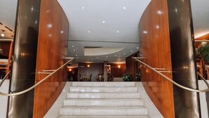A modern hotel lobby with a marble staircase, wooden paneling, and a reception desk.