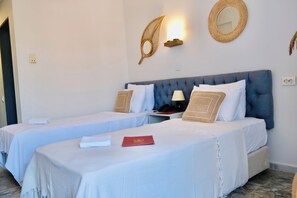 A hotel room with two beds, a blue headboard, white bedding, a red booklet, and wall-mounted decor. - Hanedan Beach Hotel (Foça)