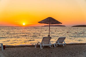 A beach scene with two lounge chairs and a beach umbrella, overlooking the ocean at sunset. - Hanedan Beach Hotel (Foça)