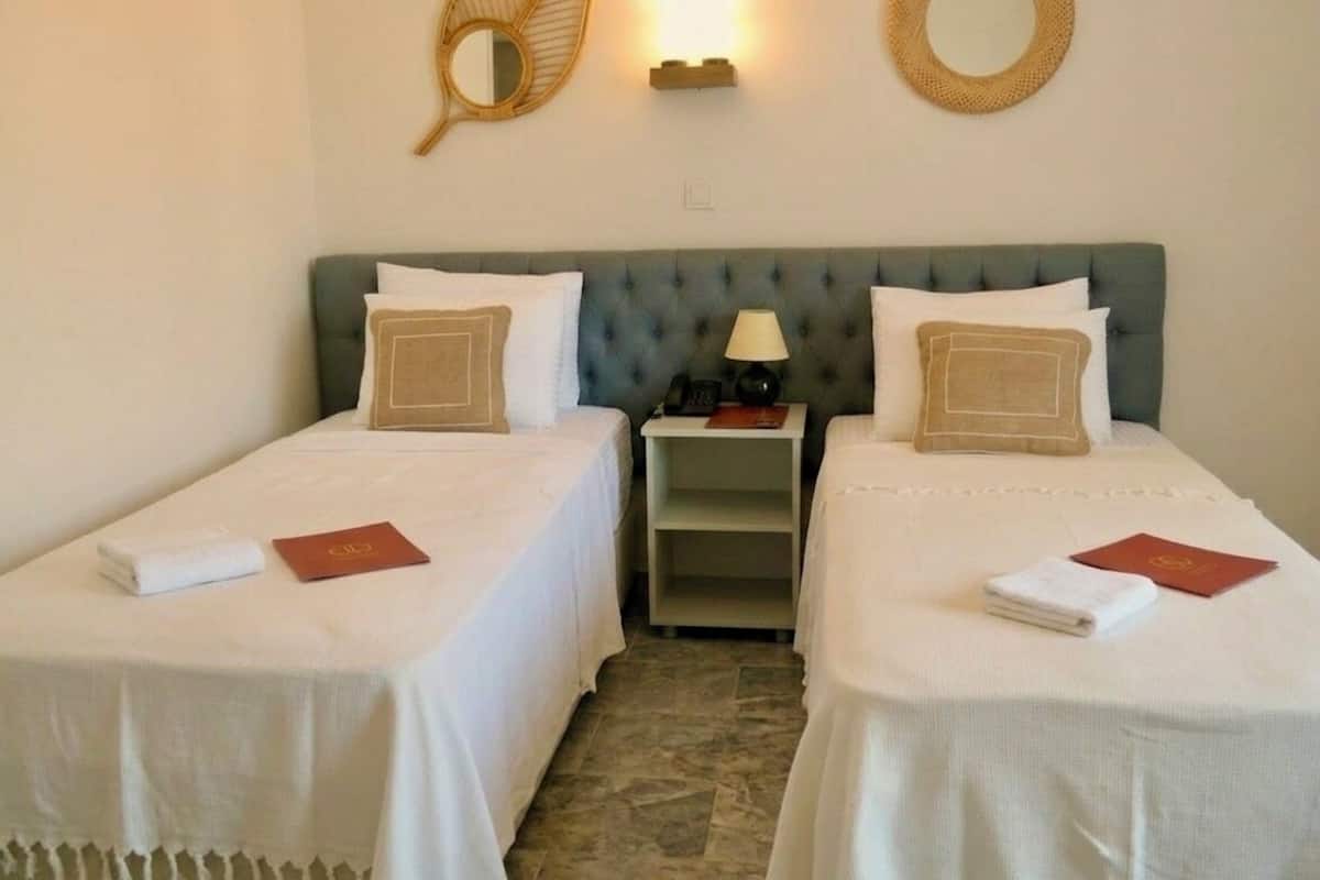 Een hotelkamer met twee eenpersoonsbedden, een nachtkastje met een lamp en decoratieve spiegels aan de muur.