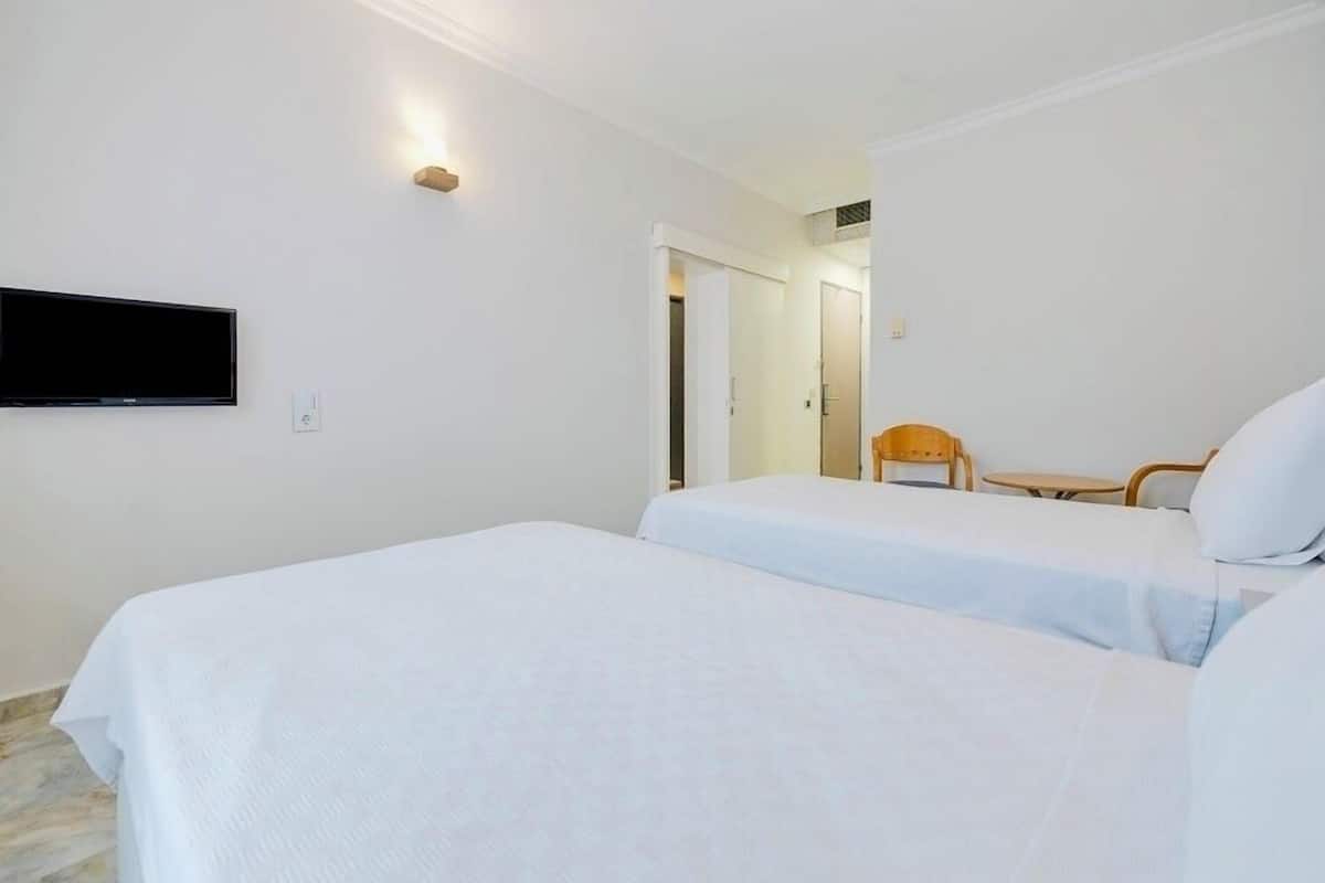 Een hotelkamer met twee bedden, een aan de muur bevestigde televisie, een stoel en een tafeltje.