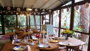 Un comedor con mesas y sillas de madera, rodeado de grandes ventanales y platos decorativos.