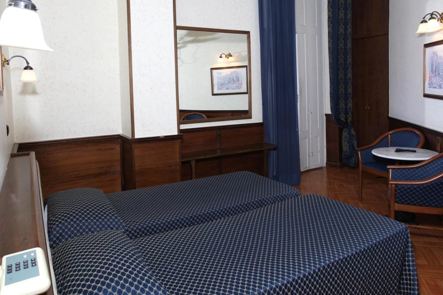Une chambre d’hôtel comprenant un lit, une table de chevet, une lampe, une chaise et une petite table.