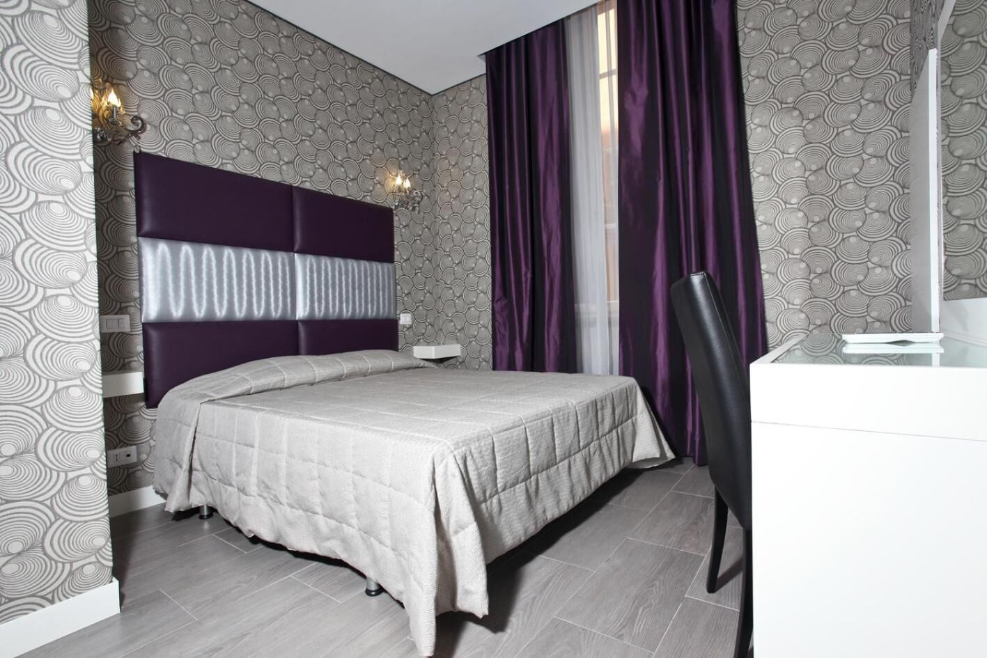 A modern hotel room with a large bed, a desk, and a chair.
