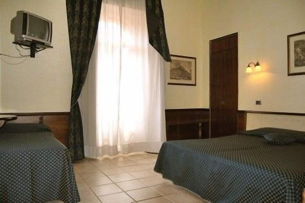 Quarto de hotel com duas camas de solteiro, uma televisão, um guarda-roupa e um quadro na parede.