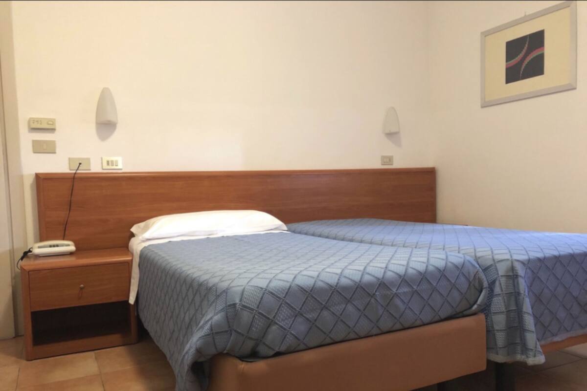 Ein Schlafzimmer mit Holz-Kopfteil, einem Einzelbett mit blauer Bettdecke, einem Nachttisch mit Telefon und einer Wandleuchte.