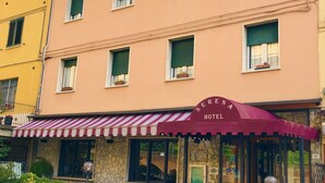 A hotel with a stone facade, a red and white striped awning, and outdoor seating. - Serena (Riolo Terme)