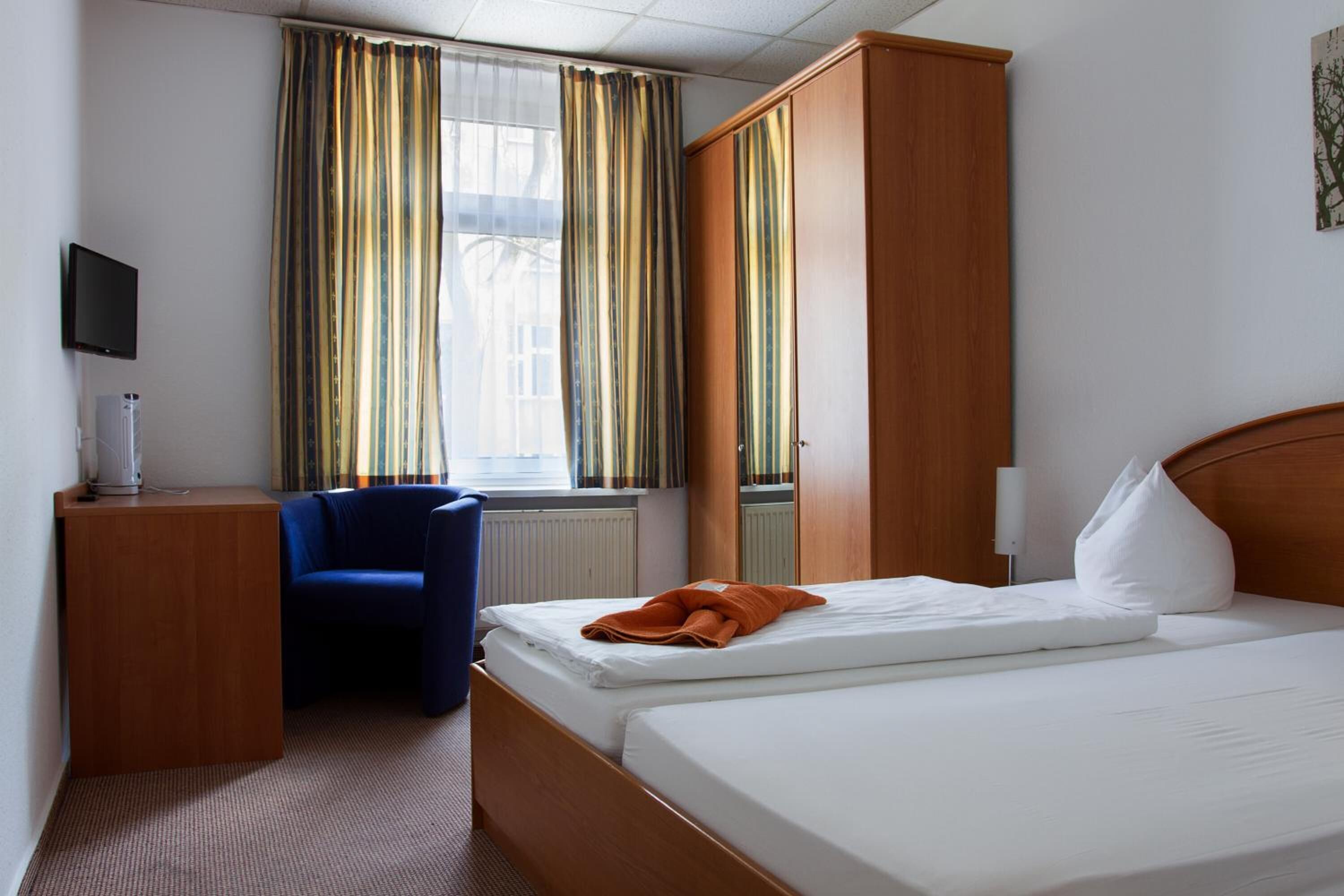Une chambre d’hôtel avec un lit, un bureau, une chaise, une télévision et une fenêtre avec des rideaux.