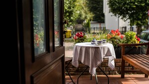An outdoor patio with a table set for two, a bench, and a view of a garden with red flowers. - Oliwa Park Residence (Gdansk)