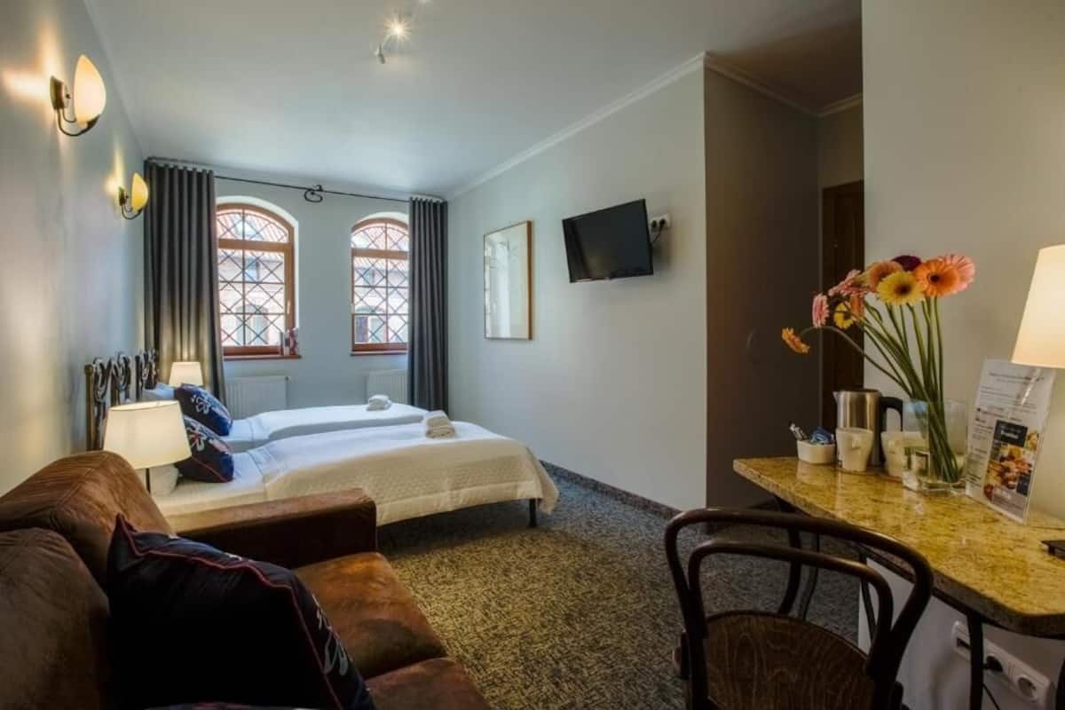 A hotel room with a bed, a desk with a lamp, a TV, and a vase with flowers.