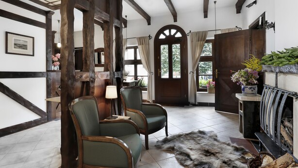 A room with exposed wooden beams, a fireplace, two green upholstered chairs, a fur rug, and a view of the outdoors through a door. - Oliwa Park Residence (Gdansk)
