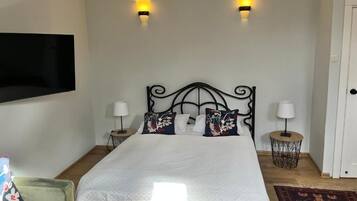Una cama bien hecha con edredón blanco, dos lámparas fijadas a la pared y un cojín decorativo.