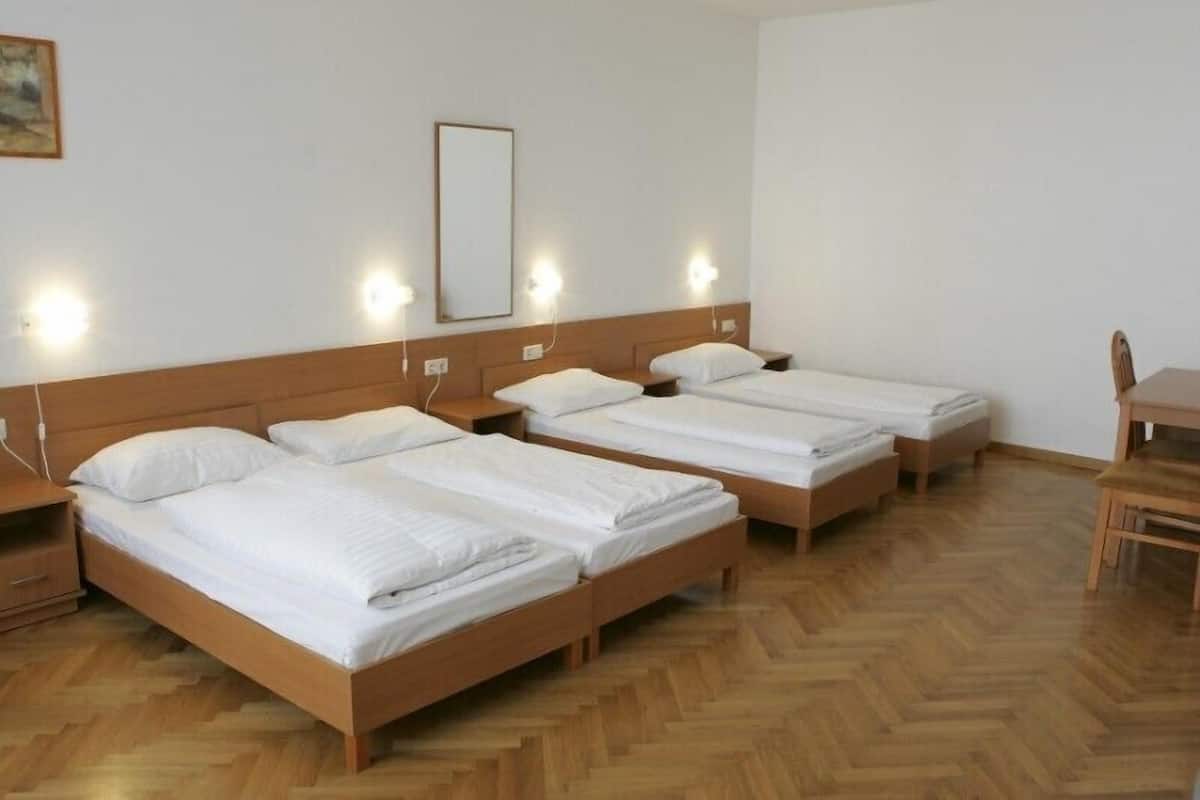 A hotel room with four single beds, wooden headboards, and bedside tables.