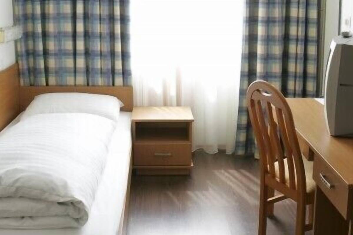 A hotel room with a bed, a desk, a chair, and a window with curtains.