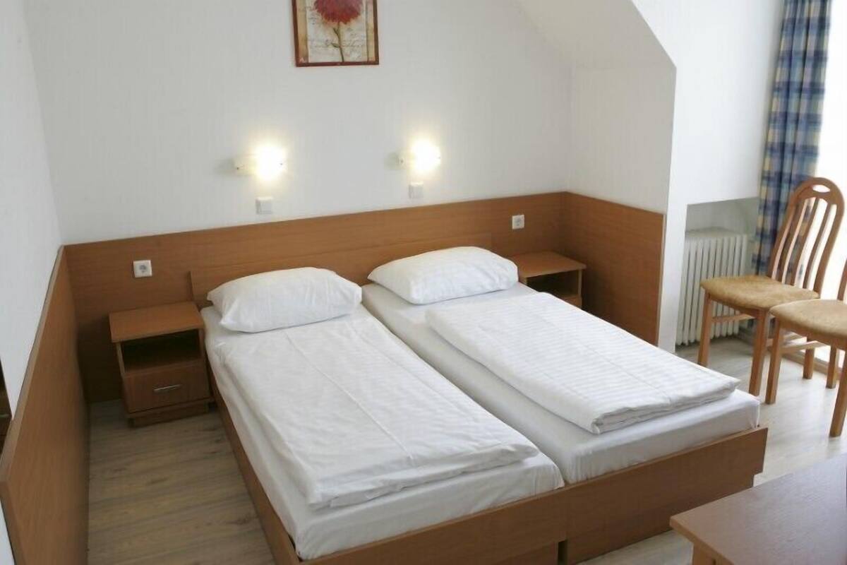 A small, neatly arranged bedroom with two single beds, a wooden headboard, bedside tables, and a chair.