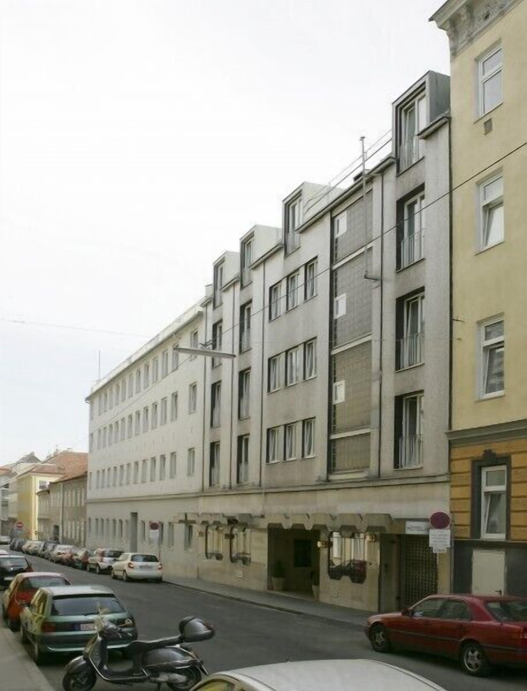 A row of multi-story buildings with a row of parked cars in front.
