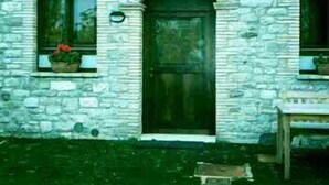A stone building with a central arched doorway, two windows with flower boxes, and a small table outside. - Barberani (Baschi)