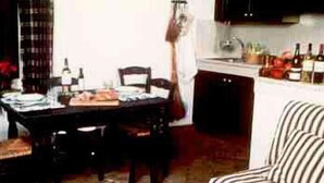 A dining area with a table set for two, a chair, and a striped sofa. - Barberani (Baschi)