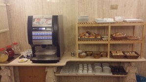 A coffee machine with multiple drink options, a counter with plates, cups, and a variety of baked goods.